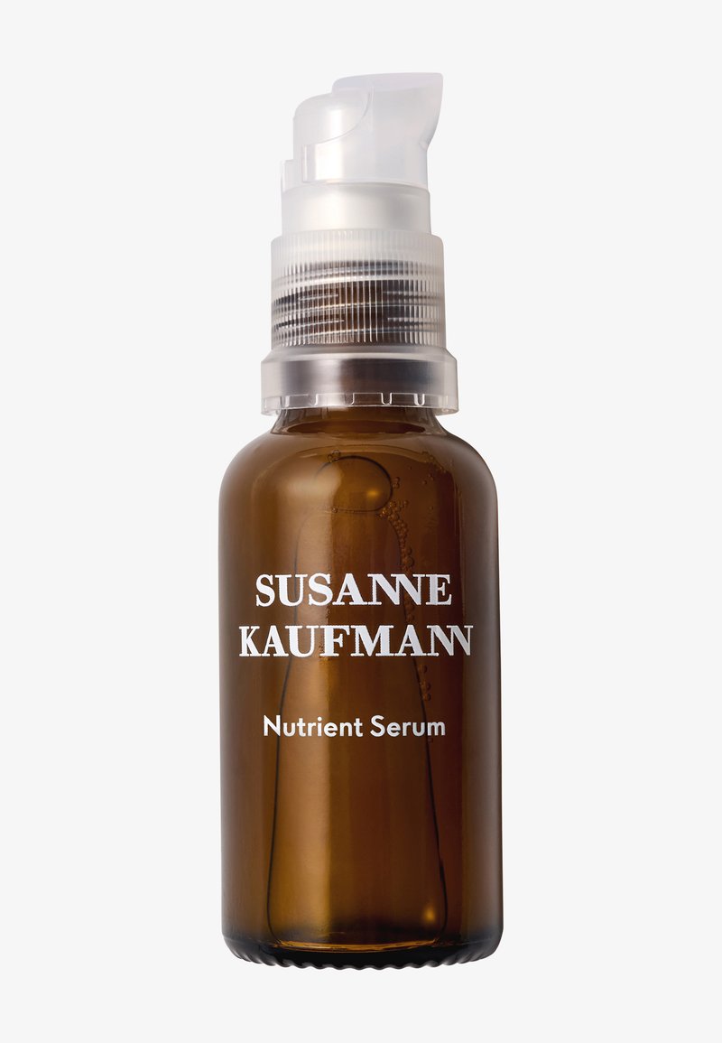 Bouteille en verre brun avec un bouchon-pompe en plastique transparent. L'étiquette présente un texte blanc : "SUSANNE KAUFMANN" et "Sérum Nutritif". Surface lisse.