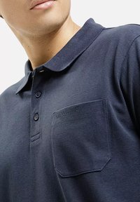 Granatowa koszulka polo wykonana z teksturowanej tkaniny, z kołnierzykiem, dwoma guzikami oraz kieszonką na piersi z subtelnym detalem brandingowym.