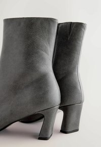 Szare botki za kostkę z sztucznej skóry o teksturowanym wykończeniu, z okrągłym noskiem i średnim obcasem w kształcie bloku. Widoczne szwy po bokach.