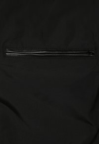 Tissu noir avec une poche zippée horizontale bordée de cuir noir, fermée contre la surface.