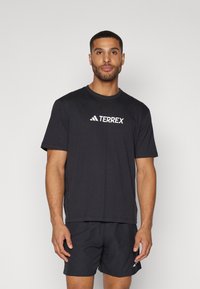 Sort kortærmet T-shirt lavet af bomuld med rund hals, prydet med et hvidt "TERREX" logo på tværs af brystet. Bæres med mørke shorts.