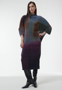 Gebreide, oversized jurk met een kleurverloop van blauw naar paars, met ribbelstructuur en verlaagde schouders. Gecombineerd met zwarte laarzen tot boven de dijen.