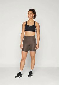 Svart sportsbh med hvite striper, kombinert med høyt belte brune shorts. Modell med svarte treningssko og hvite ankelstrømper.