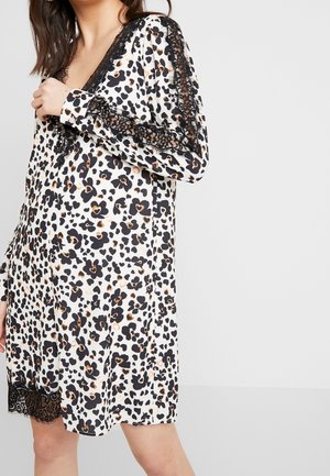 Frau trägt ein weißes Kleid mit schwarzem und beigem Leopardenmuster, das schwarze Spitzenbesätze entlang des Ausschnitts, der Ärmel und des Saums aufweist.