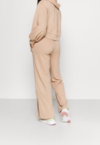 Persona che indossa pantaloni tuta beige a gamba larga con aperture laterali e una felpa abbinata, abbinati a sneaker bianche con suole rosa.
