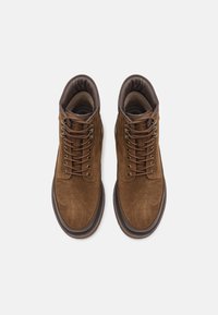 Brune suedeboots til anklene med runde tåspisser, metallhull og mørkebrune snørebånd; polstret krage og en teksturert gummisåle.