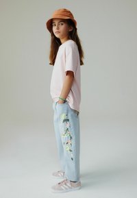 Maglietta rosa chiaro, jeans di jeans blu con ricami floreali vivaci, abbinati a sneakers rosa e cappello a secchiello arancione.