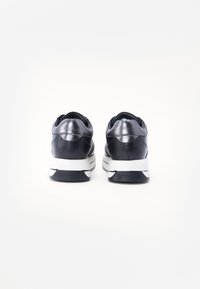 Zwarte leren sneakers met een glanzende afwerking, voorzien van een witte zool en merkname op de hiel. Soepele textuur en afgerond ontwerp.