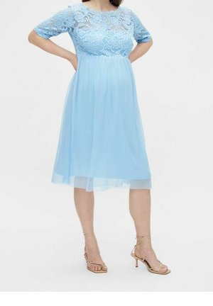 Robe bleu clair avec manches courtes en dentelle, superposition semi-transparente et jupe midi fluide. Associée à des talons beige à lanières.