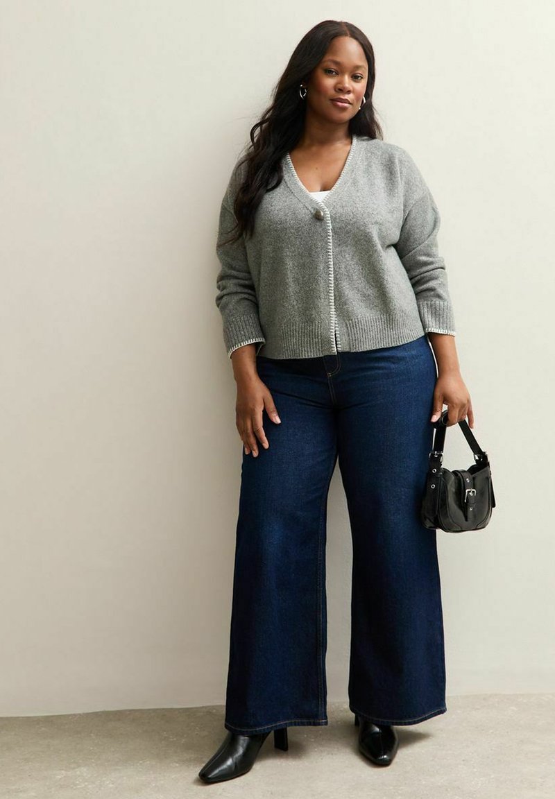 Cardigan grigio a maglia con scollatura a V e chiusura a bottoni, abbinato a jeans in denim blu scuro a gamba larga. Accessoriato con una piccola borsa nera.