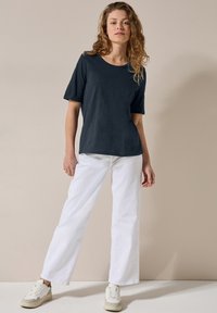 Námornícké tričko s krátkým rukávem a kulatým výstřihem, spárované s bílými rovnými džíny. Nosené s světlými teniskami.