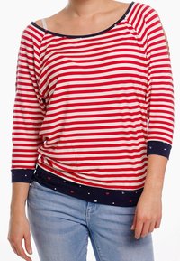 Rød og hvid stribet bluse med lange ærmer, scoop neckline og marineblå detaljer. Har udskæringer ved skuldrene og mønstret kant.