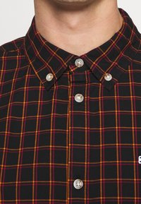 Schwarz karierte Hemd mit orange- und pinkfarbenen Karo-Mustern, klassischer Kragen, Knopfverschluss vorne mit weißen Knöpfen und besticktem Detail.