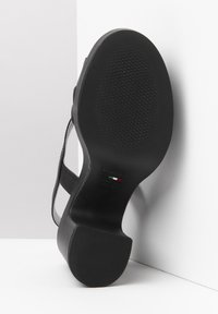 Black high-heeled shoe with a smooth leather upper and rubber sole, featuring a textured grip pattern and minimalistic design.