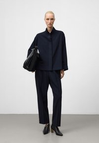 Camicia azzurra oversize con bottoni, a righe orizzontali, abbinata a pantaloni tapered coordinati e mule nere con tacco alto. Porta una borsa nera.