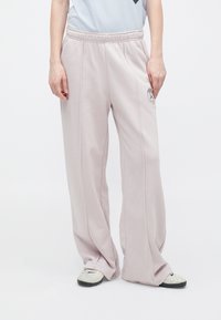 Lyserøde sweatpants med løs pasform, elastisk talje, sidelommer og et logo-patch på venstre lår. Blødt stof, glat tekstur.