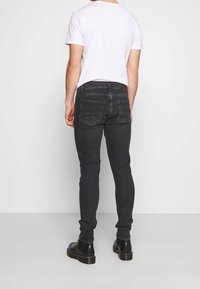 Svarta slim-fit jeans med en jämn yta, fem fickor och synlig sömnad. Bärs med en enkel vit t-shirt och svarta stövlar.