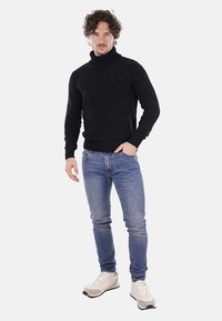 Maglione a collo alto neri, slim fit, abbinato a jeans azzurri chiari e sneakers bianche. Presenta polsini e orlo a costine.