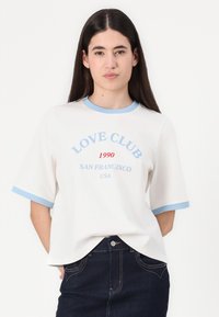 Balta marškinėliai su šviesiai mėlynu raišteliu aplink kaklą ir rankoves, ant kurių spausdinamas tekstas "LOVE CLUB 1990 SAN FRANCISCO USA" mėlyna ir raudona spalvomis. Klasikinio kirpimo.