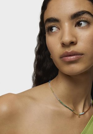 Collana di perline colorate con piccole perline rotonde nelle tonalità di blu, verde e marrone, con un accento dorato vicino al gancio su una spalla nuda.