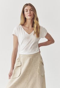 Biela krátka rukávová T-shirt s výstrihom do V, skombinovaná s svetlobéžovou ľanovou sukňou, ktorá má dve veľké nákladné vrecká, hladkú textúru a uvoľnený strih.