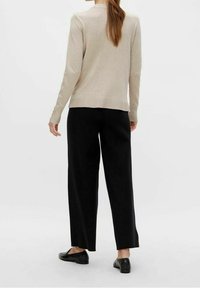Ljusbeige långärmad tröja med rundad halsringning, i kombination med löst sittande svarta byxor och svarta platta skor. Slät textur, avslappnad design.