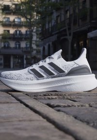 Baskets blanches et grises avec des rayures noires sur une rue pavée dans un cadre urbain sous une lumière douce du jour.