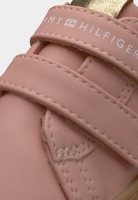 Ροζ δερμάτινο παπούτσι με δύο ρυθμιζόμενους ιμαντες Velcro. Διαθέτει λευκή ραφή και χρυσή λεπτομέρεια στη φτέρνα. Ορατό λογότυπο στο ιμάντα.