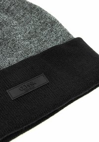 Szaro-czarna dzianinowa czapka beanie z podwiniętym mankietem, na którym znajduje się czarna prostokątna metka z napisem "OCHNIK EST. 1989."