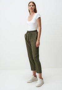 Bodysuit blanc à manches courtes associé à un jogging tapered vert olive avec une taille élastique et des poches latérales, porté avec des sneakers blanches.