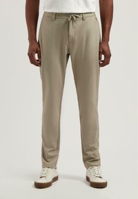 Beige, taps toelopende broeken met een trekkoord in de taille, met een subtiele textuur en streepjespatroon, gecombineerd met witte sneakers en lichtbruine zolen.