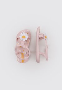 Sandalias de playa rosas con una correa texturizada, adornadas con una flor blanca y un centro amarillo, que presentan un patrón floral en la suela.