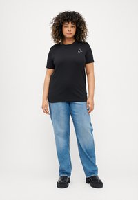 Μαύρο t-shirt κοντό μανίκι με στρογγυλή λαιμόκοψη και μικρό λευκό λογότυπο, σε συνδυασμό με ανοιχτό μπλε τζιν κανονικής γραμμής και μαύρες πλατφόρμες.