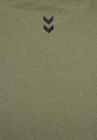 Olijfgroene getailleerde shirt gemaakt van ribbelstof, met twee zwarte chevronaccenten nabij de halslijn. Gladde textuur overal.