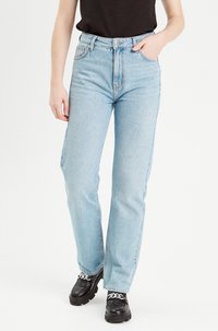 Light blue denim straight-leg jeans with a high waist, five pockets, and a zipper fly. Worn with black platform shoes.
