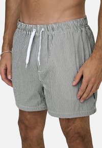 Gestreifte Badeshorts mit einem grau-weißen Muster, elastischem Bund mit Kordelzug und seitlichen Taschen. Strukturierter Stoff, lockere Passform.