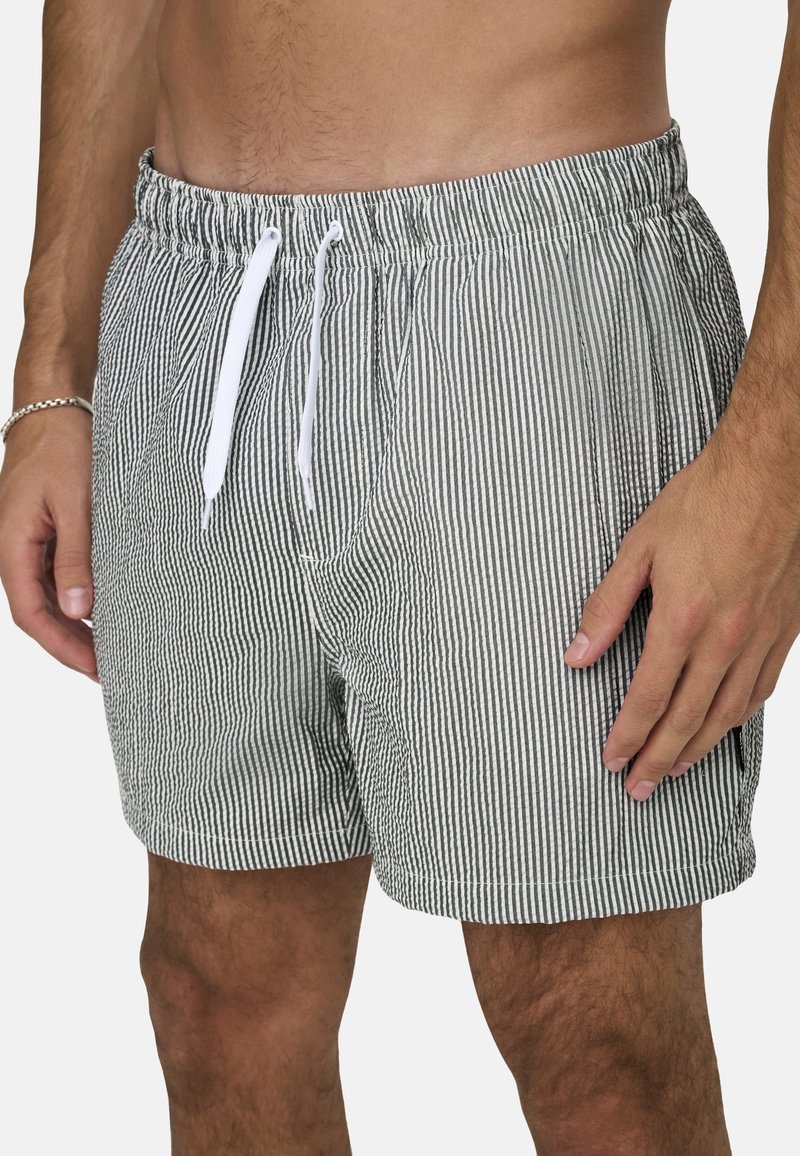 Gestreifte Badeshorts mit einem grau-weißen Muster, elastischem Bund mit Kordelzug und seitlichen Taschen. Strukturierter Stoff, lockere Passform.