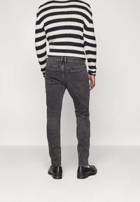 Svart och vit randig tröja i stickad material, ihop med grå denimbyxor. Byxorna har bakfickor och en avsmalnande passform.