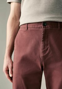 Pantalones de algodón color marrón oscuro con una textura suave, que cuentan con cierre de botón estándar, trabillas para cinturón y costuras en los bolsillos. El fit parece ser entallado.