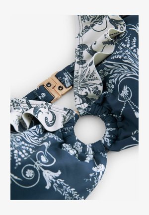 Tissu floral bleu marine avec des bords froncés ; présente un fermoir en métal doré et une section élastiquée pour un ajustement et un confort optimaux.