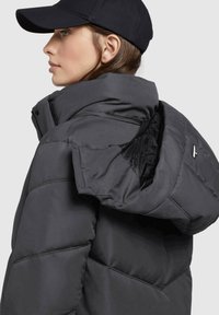Gray puffer jacket with a high collar and hood, featuring a quilted texture, zip closure, and black interior lining.