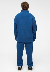 Blauwe donzige fleece pullover met een hoge kraag en een relaxte fit, gecombineerd met bijpassende blauwe fleecebroek, beide met een zachte textuur.