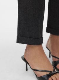 Črne po meri krojene hlače z rahlim vzorcem, zavihane na robu, kombinirane s črnimi sandali s peto in trakovi, ki imajo majhen detajl s sponko.