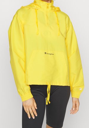 Geel hooded pullover jack met een halve rits, een voorzak en trekkoorden. Voorzien van elastische manchetten en een Champion-logo op de zak.
