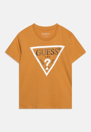 Sennepsgul kortærmet T-shirt med rund hals og hvidt trekantet GUESS-logo, inklusive teksten "U.S.A. Washed Jeans" og et spørgsmålstegn.