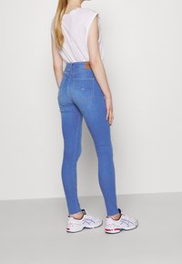 Vaqueros de tiro alto en color azul, confeccionados en denim, con un ajuste ceñido, bolsillos traseros y una etiqueta de marca de cuero en la cinturilla.