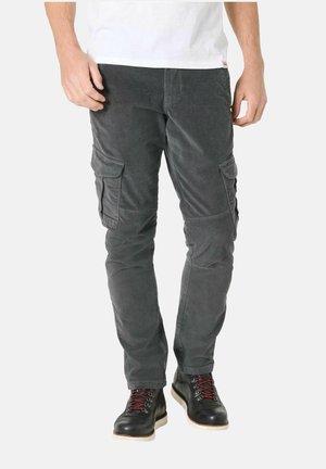 Man wearing dark gray corduroy cargo pants and black boots with red laces, standing against a plain white background.