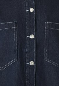Mörk denimskjorta med silverknappar, två bröstfickor med kontrasterande sömmar och en strukturerad tygyta.