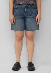 Shorts en denim bleu foncé avec un ourlet effiloché. Associés à un t-shirt graphique et des chaussures noires à enfiler pour un look décontracté.