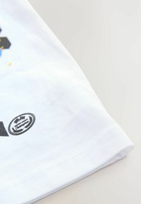 White cotton t-shirt with a rounded neckline, featuring a black and colorful graphic print on the left side, and a circular logo near the hem.